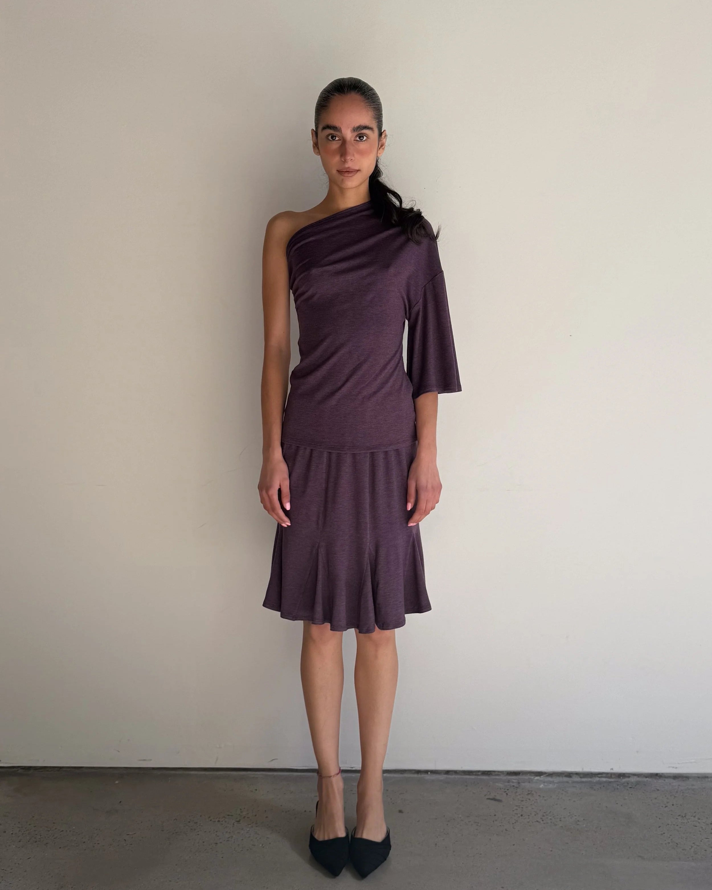 Woman wearing a one-shoulder purple dress against a plain background