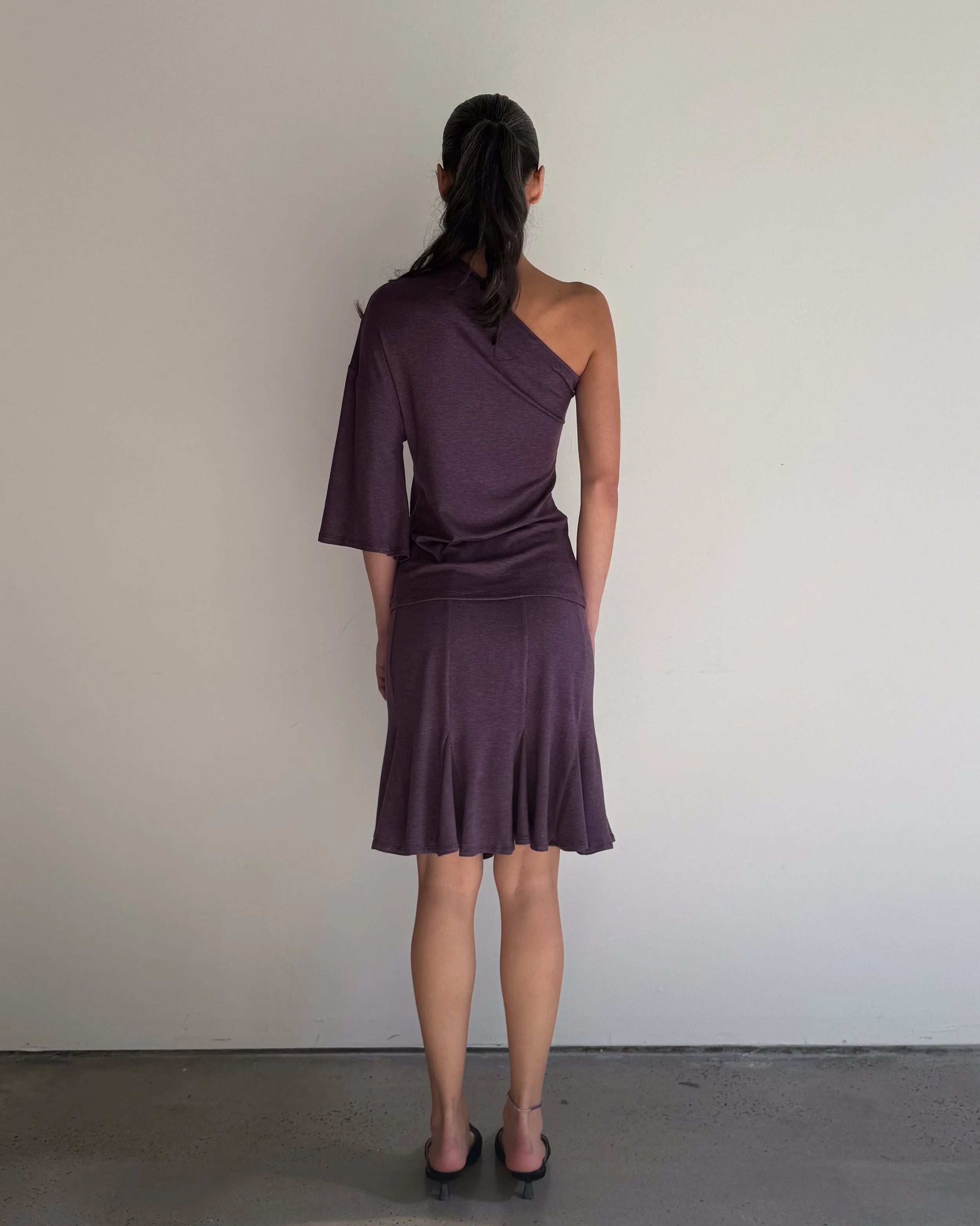 Woman wearing a one-shoulder purple dress against a plain background