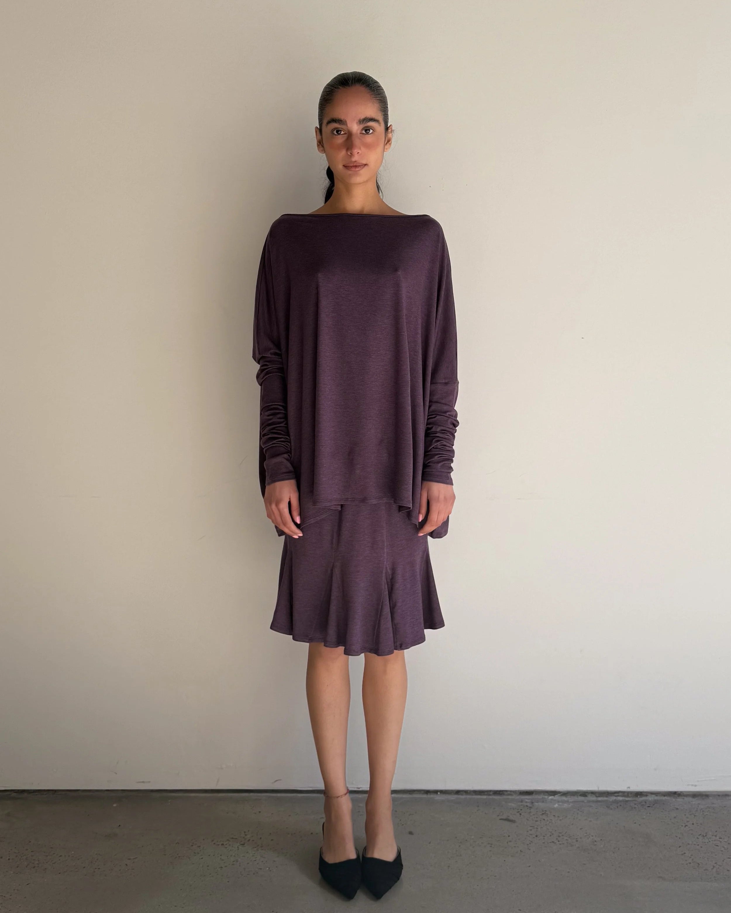 Woman wearing a long-sleeve, dark purple dress against a plain background