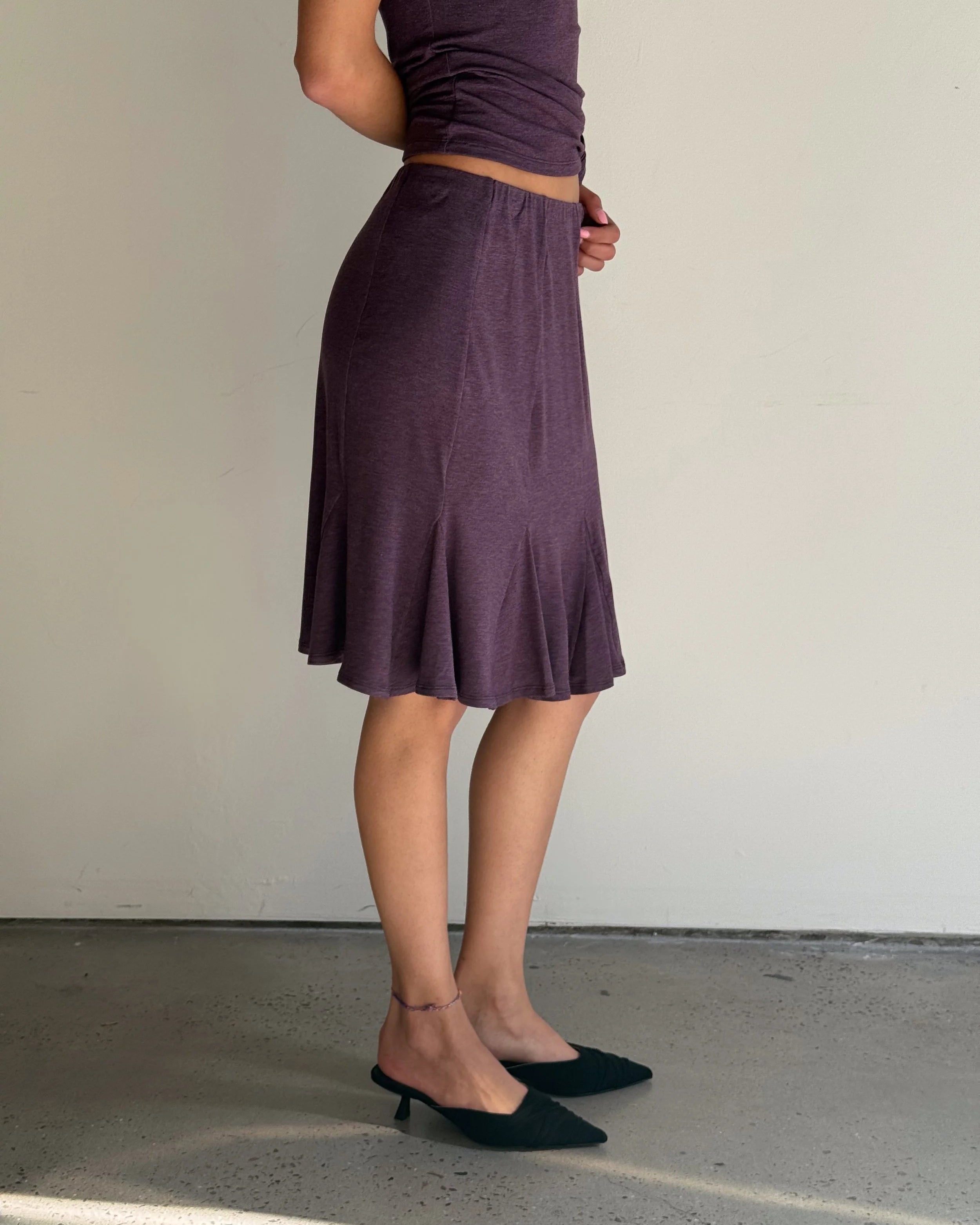 Person wearing a purple skirt and top against a plain background