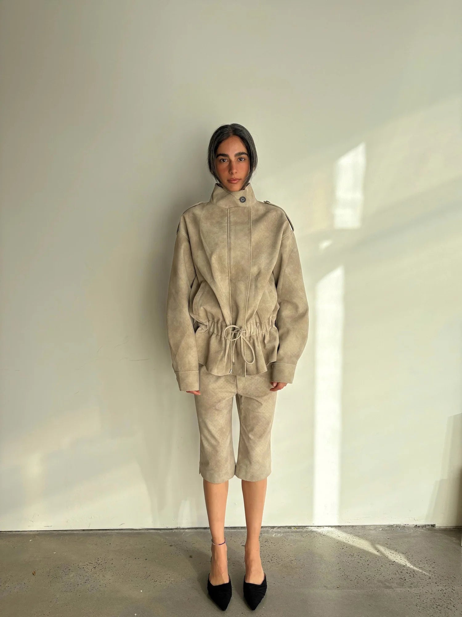 Person wearing a beige outfit standing against a plain wall.