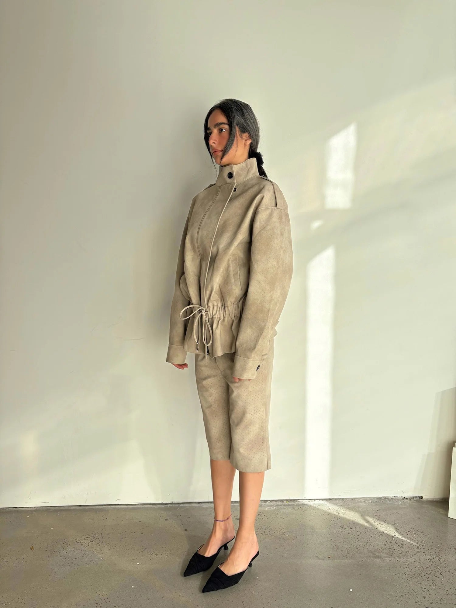 Person wearing a beige outfit standing against a white wall.