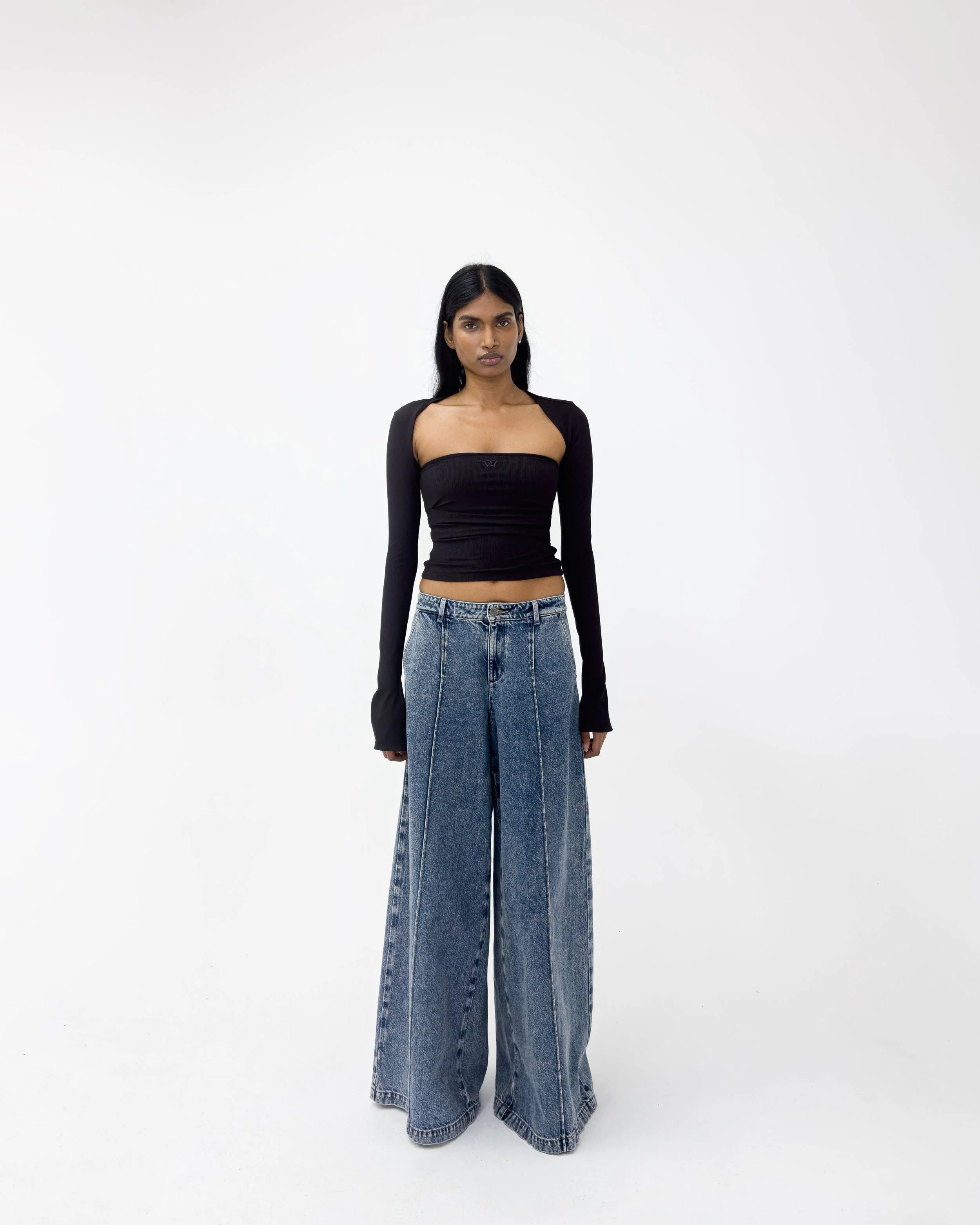 Woman wearing a black long-sleeve top and blue wide-leg jeans on a white background