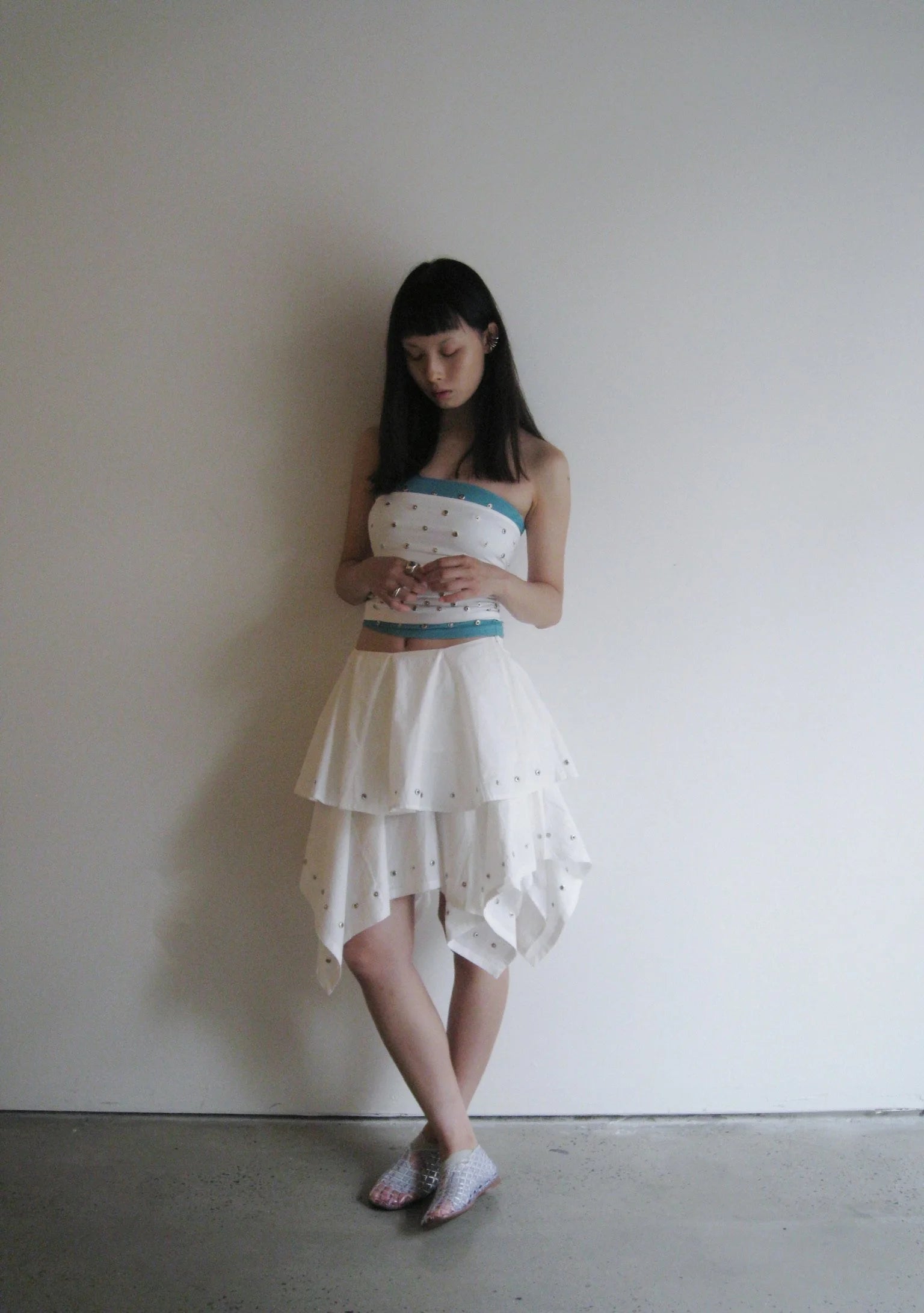 Woman wearing a strapless top and white skirt with a pattern, standing against a plain wall.