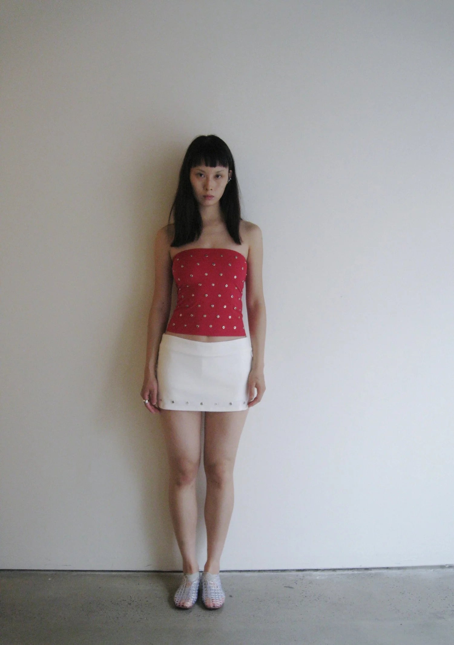 Woman wearing a red top with white polka dots and a white skirt against a plain background
