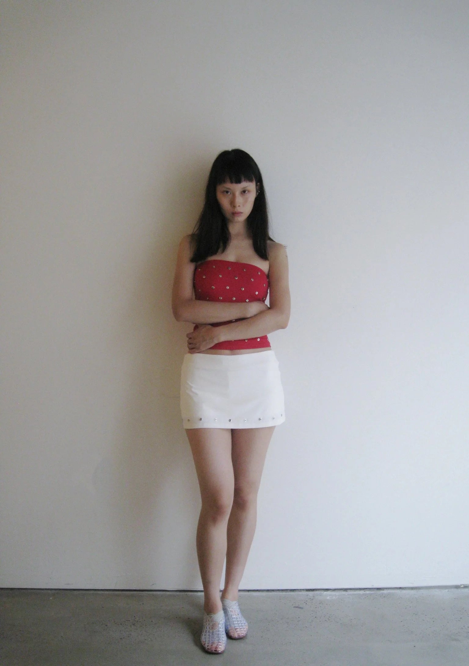 Woman wearing a red top and white skirt against a plain background