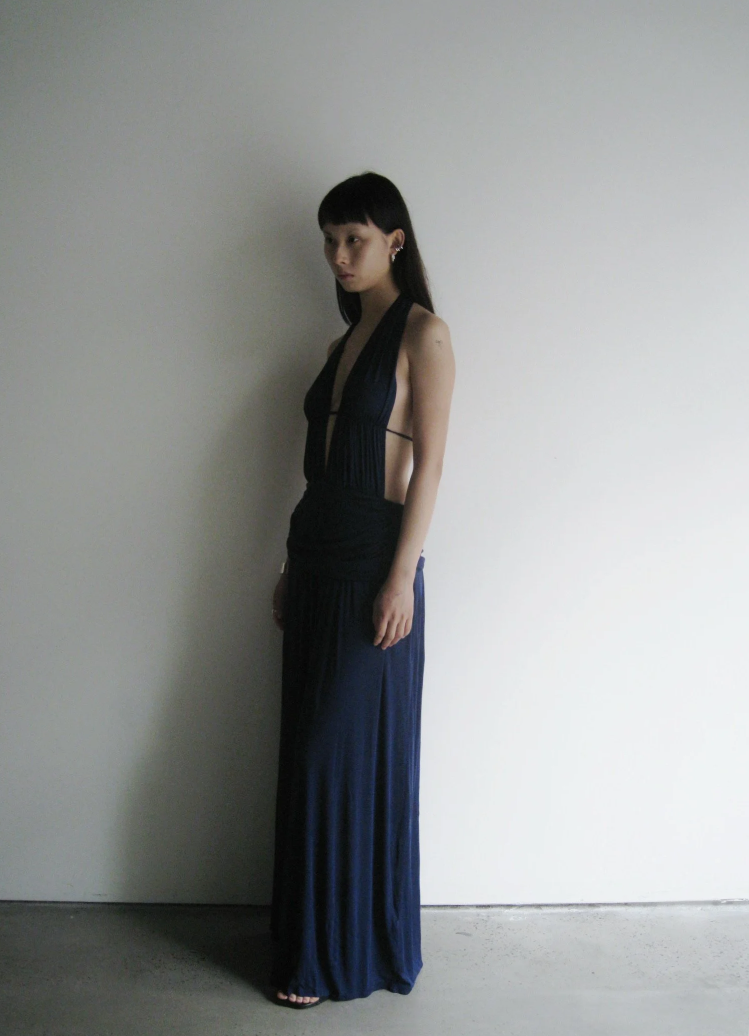 Woman wearing a long dark blue dress against a plain white wall.