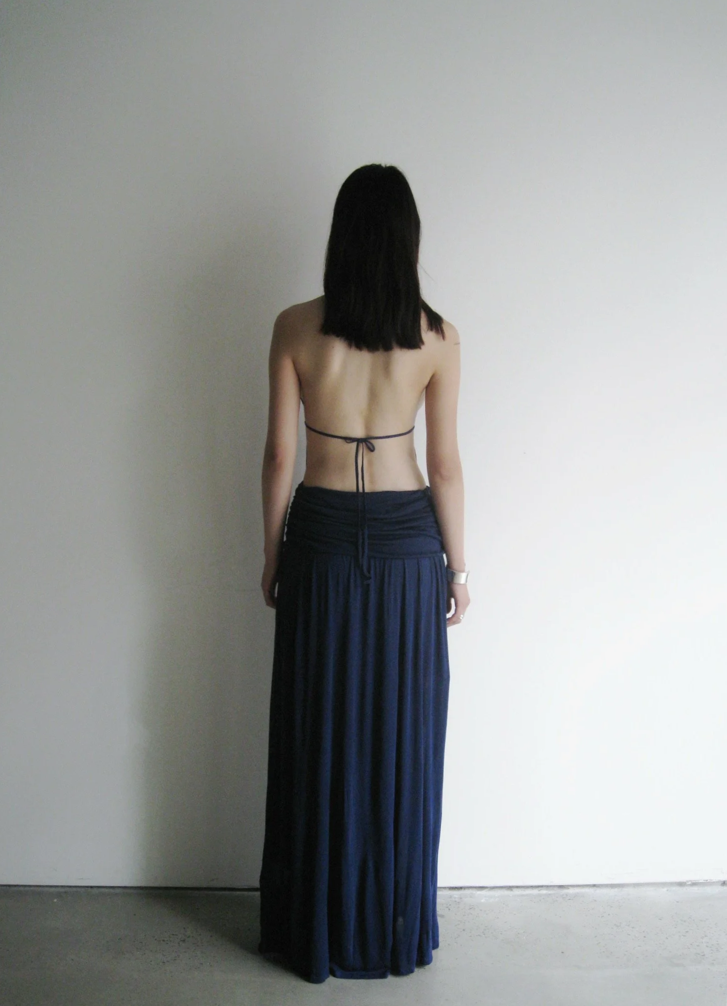Person wearing a long dark blue dress with a minimalistic design against a plain background