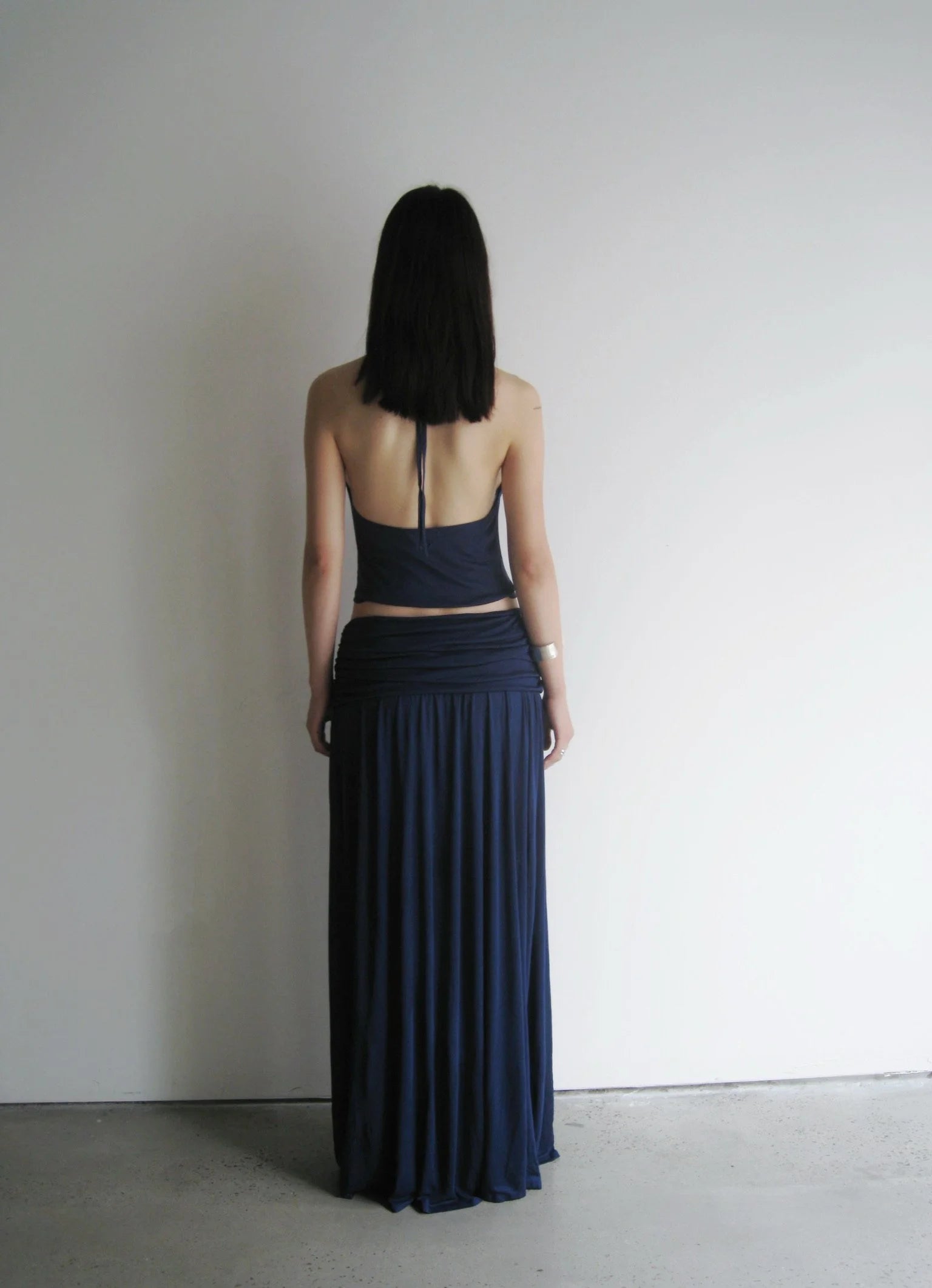 Person wearing a dark blue two-piece outfit standing against a plain white wall.