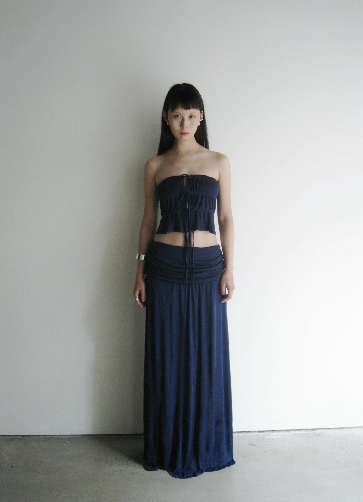 Woman wearing a dark blue strapless top and long skirt against a plain background