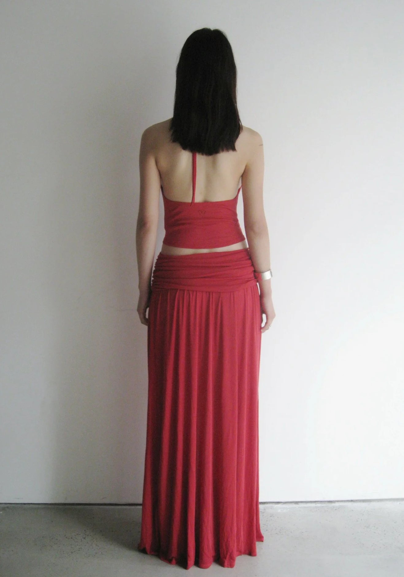 Person wearing a red dress standing against a plain white wall.