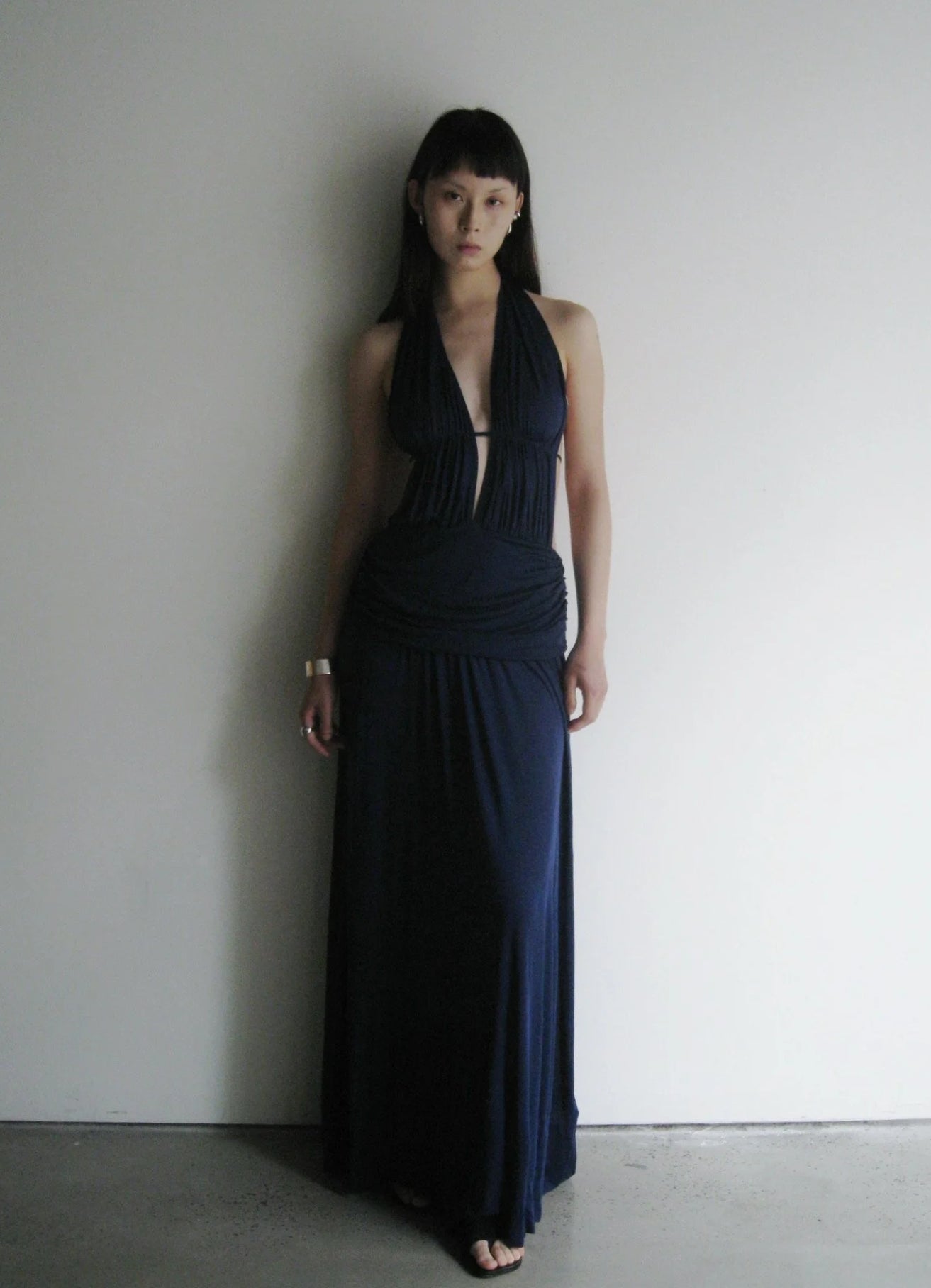 Woman wearing a dark blue halter neck dress against a plain white wall.